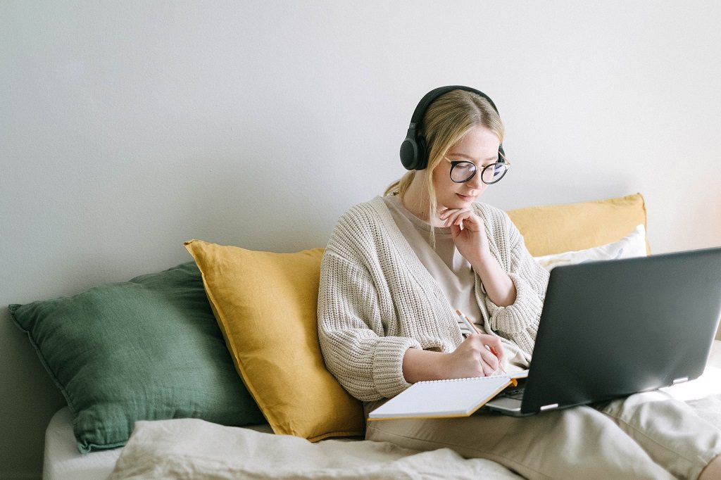 Student girl sitting in a room with her headphones and notebook ona couch