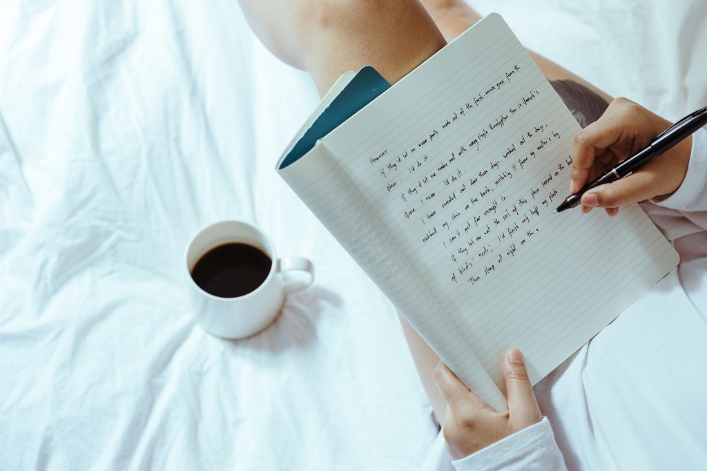 A girl writing notes and with cup of coffee on her couch 