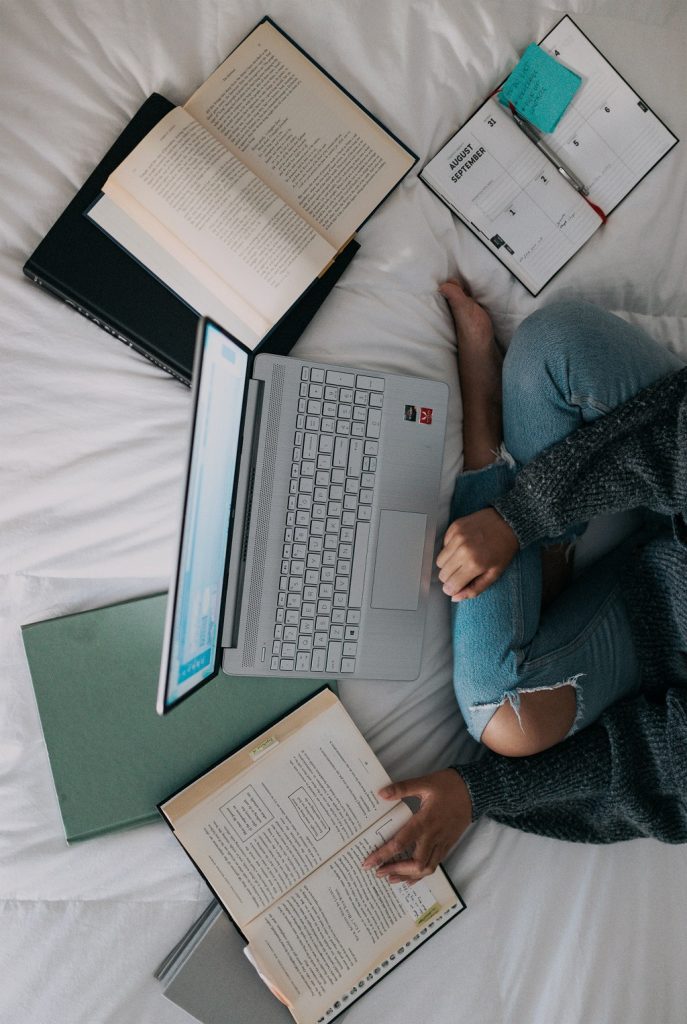 Student girl working with her notebook and books all around on her sofa, making a research