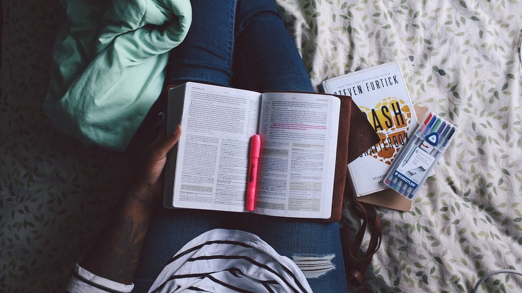  A student reading and underlying a book and making notes on a sofa.