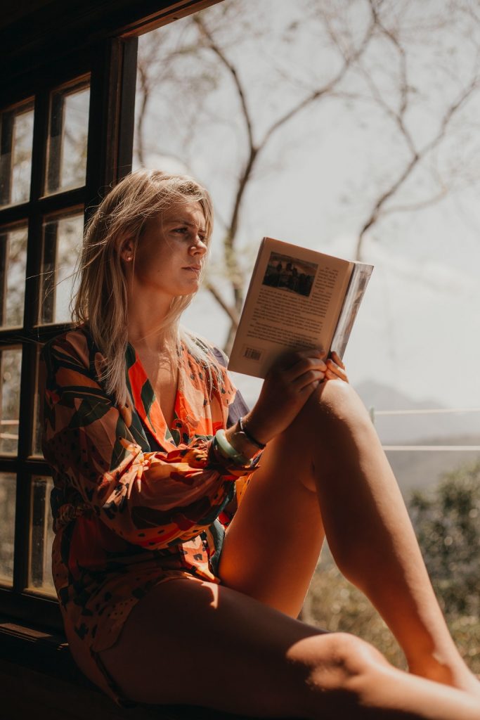 A student girl reading a book and sitting in front of open window. 